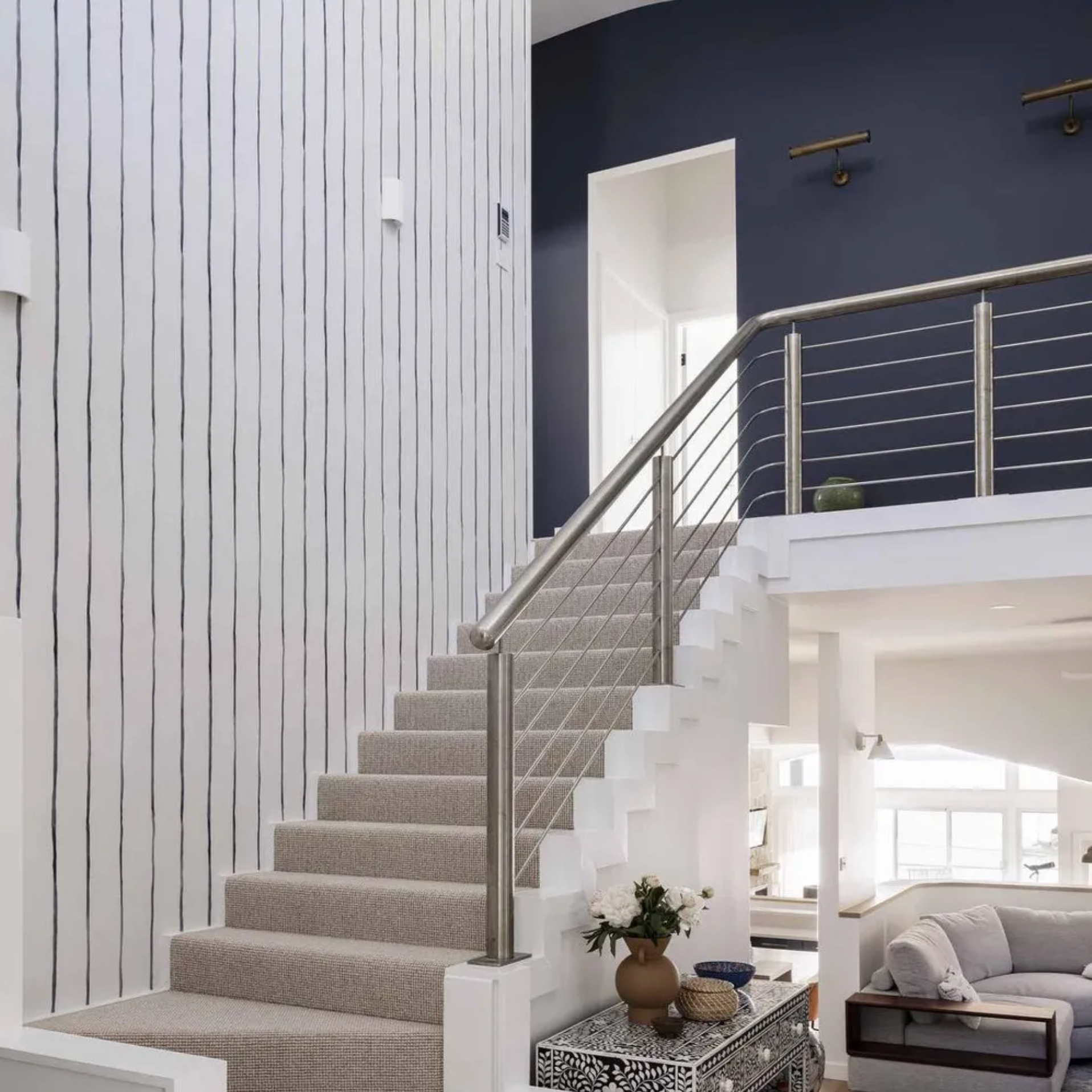 Modern staircase with white walls and a gray carpet in a home interior with picture lights.