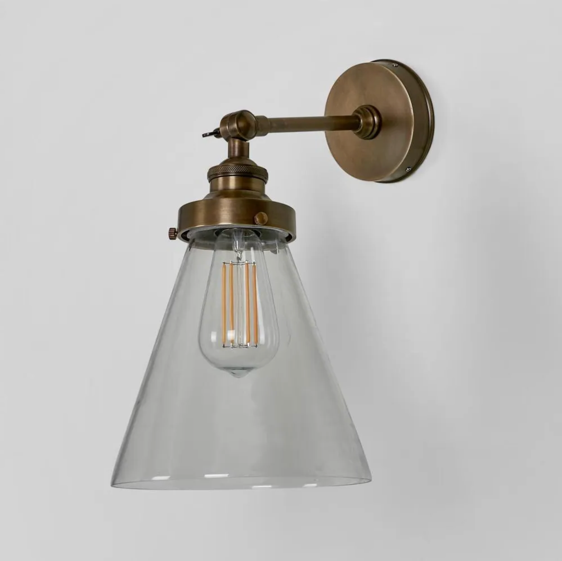 Vintage-style wall sconce with clear glass shade and brass finish on a light gray background