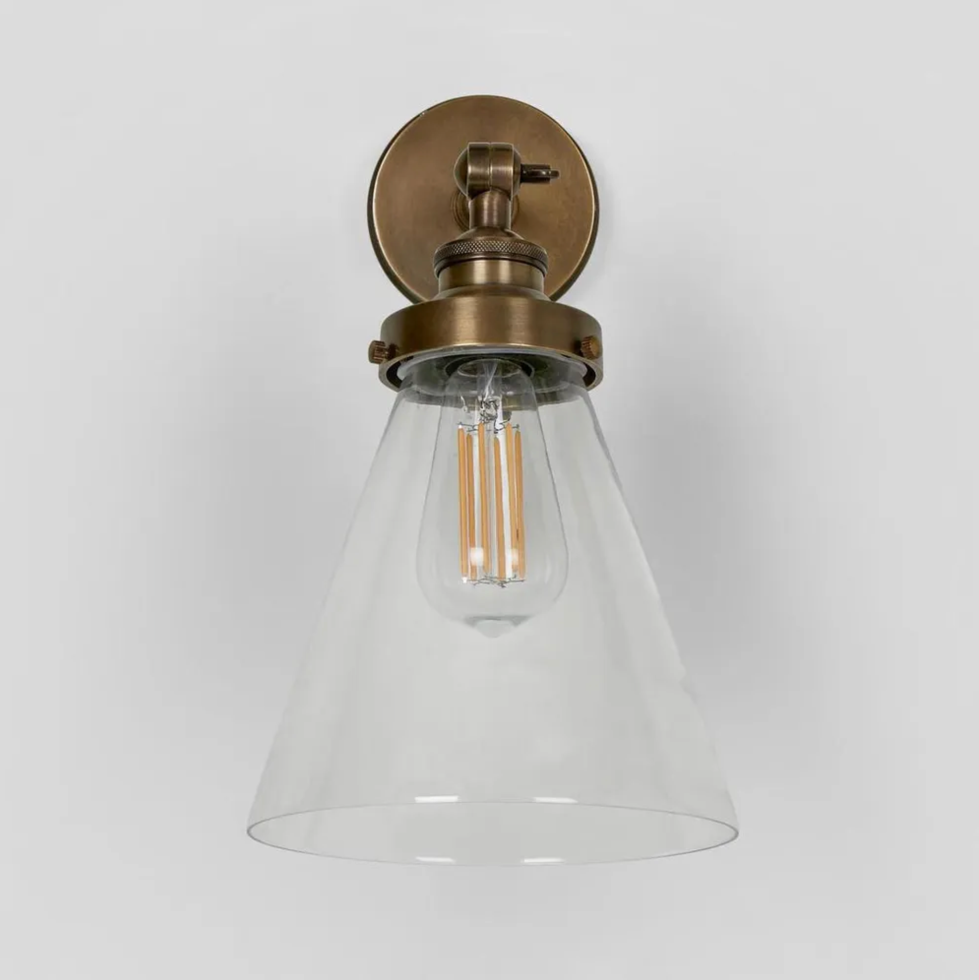 Vintage-style wall light fixture with clear glass shade and brass finish on a white background