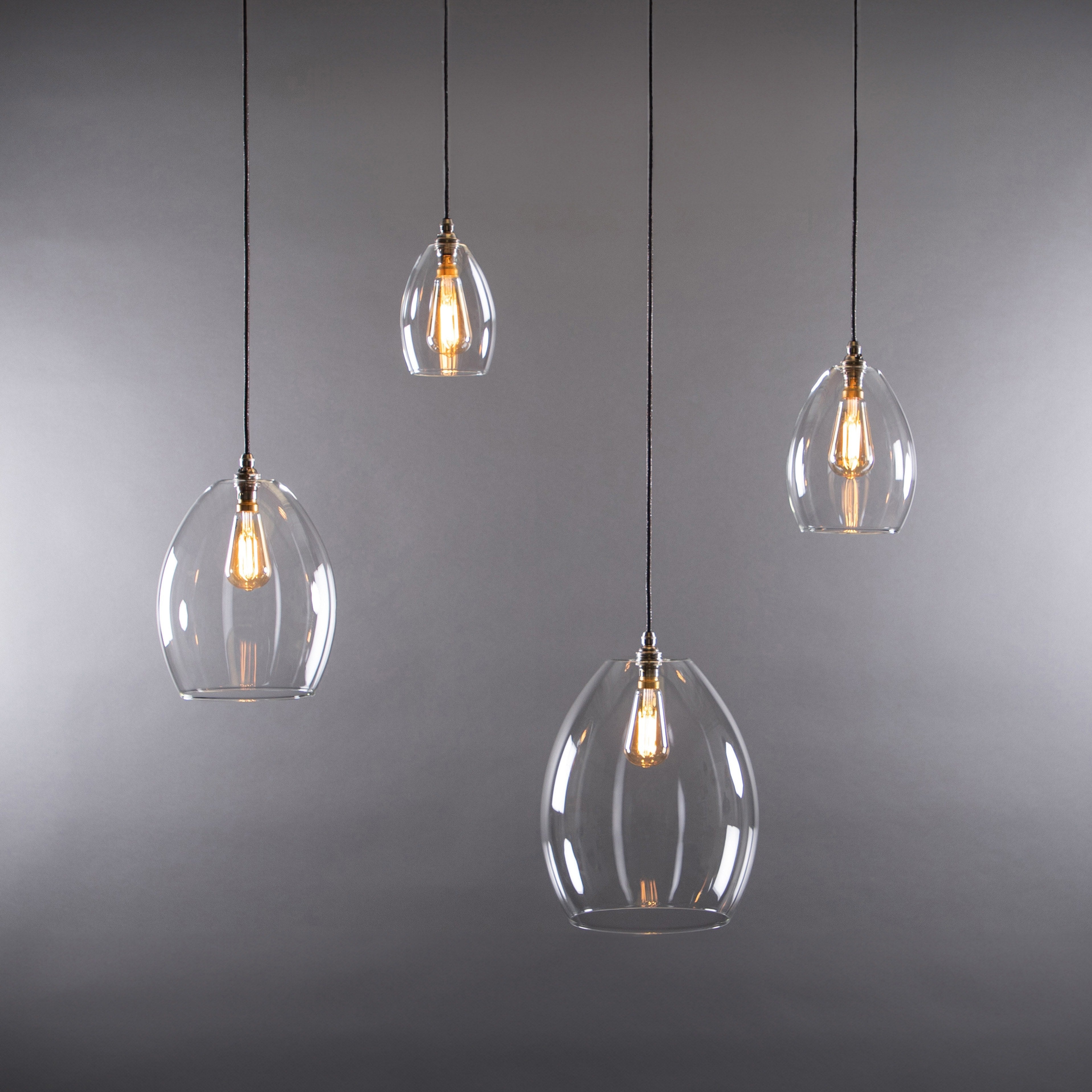 Four pendant lights with clear glass shades on a gray background
