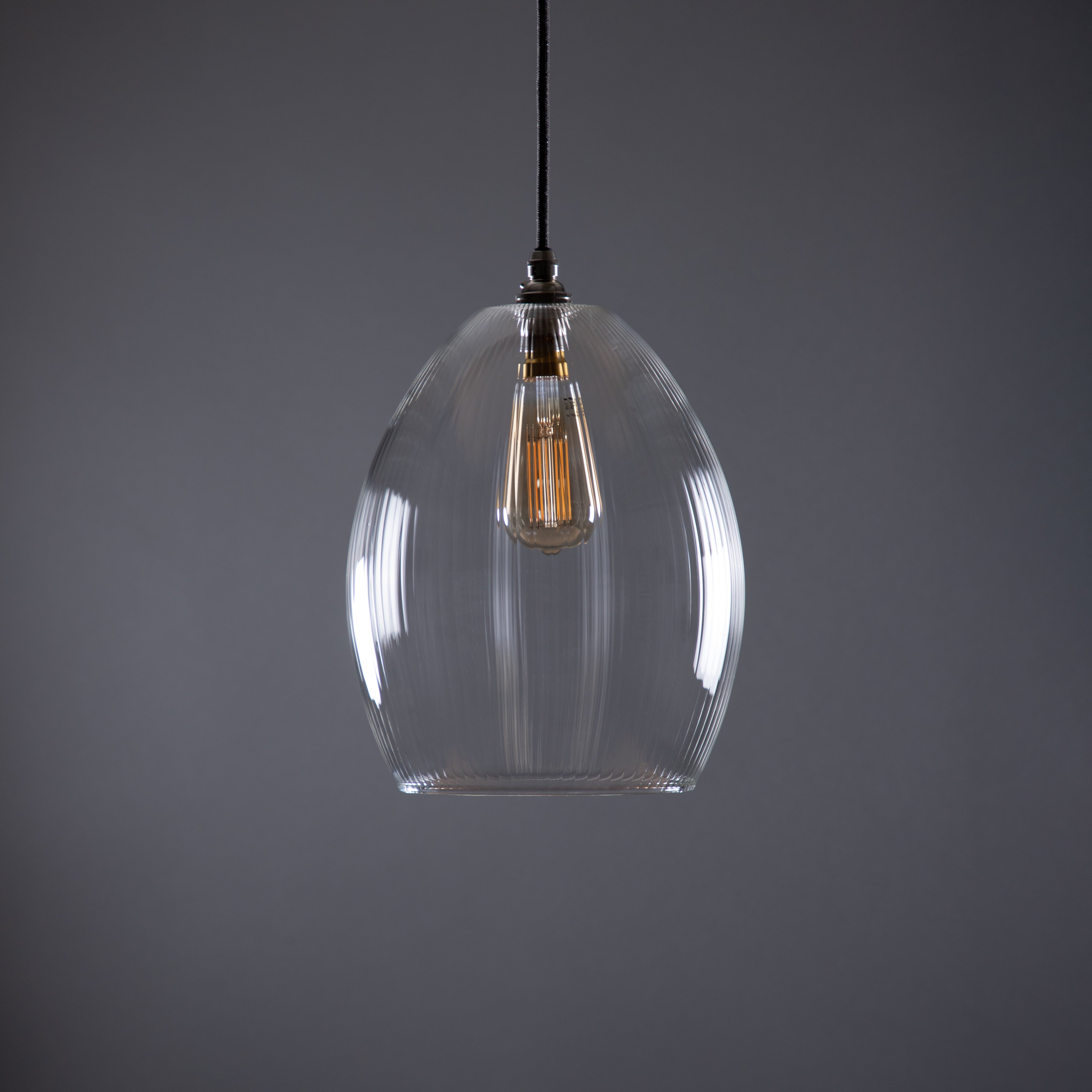 Clear glass pendant light with a visible bulb against a gray background