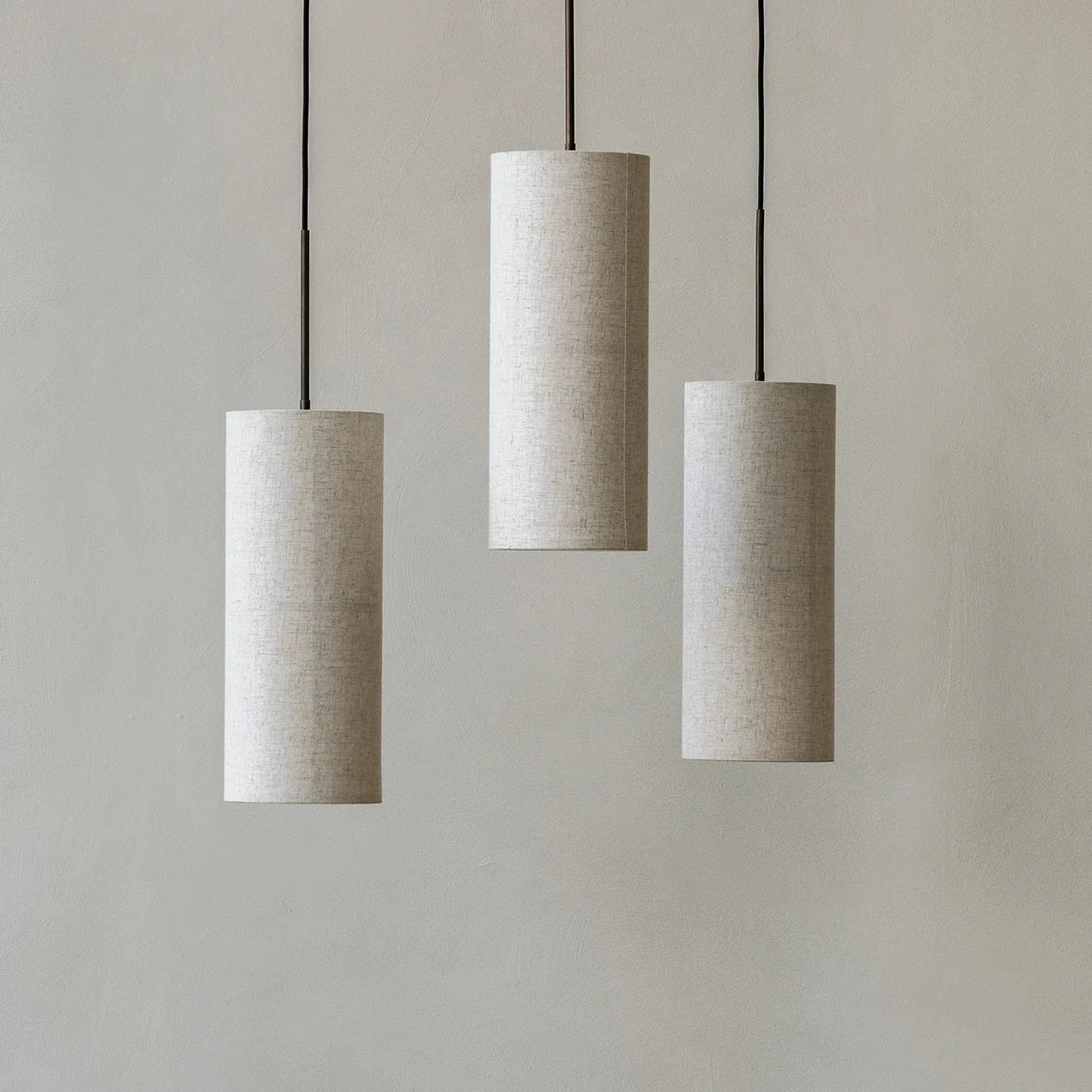 Three cylindrical pendant lights hanging above a wooden table with chairs against a plain wall.