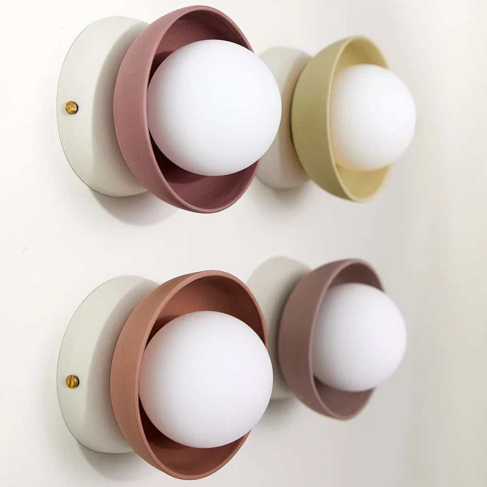 Four wall-mounted light fixtures with colorful cylindrical covers on a white background