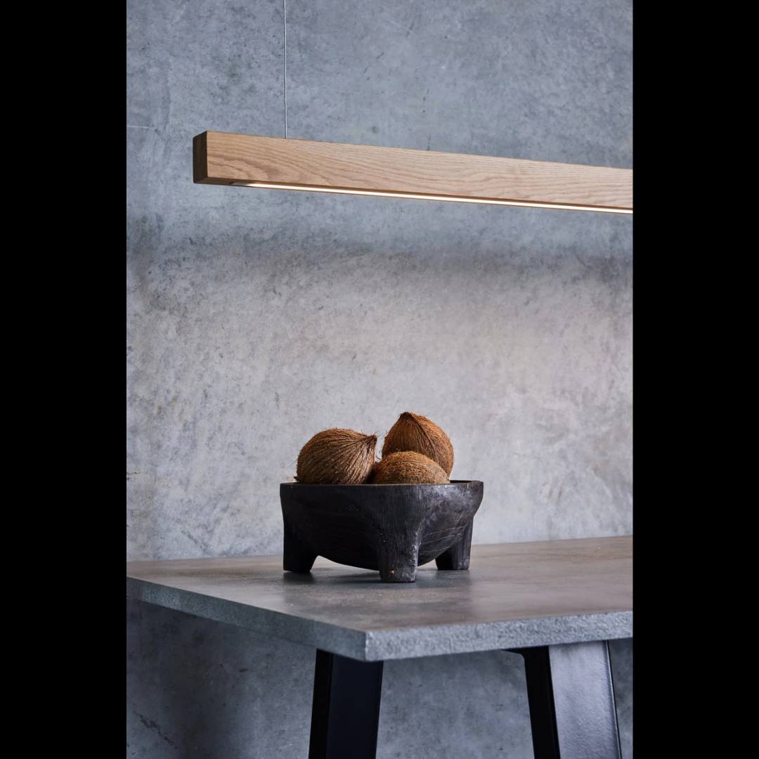 Bowl with coconuts on a table against a concrete wall with a long oak linear light fixture.