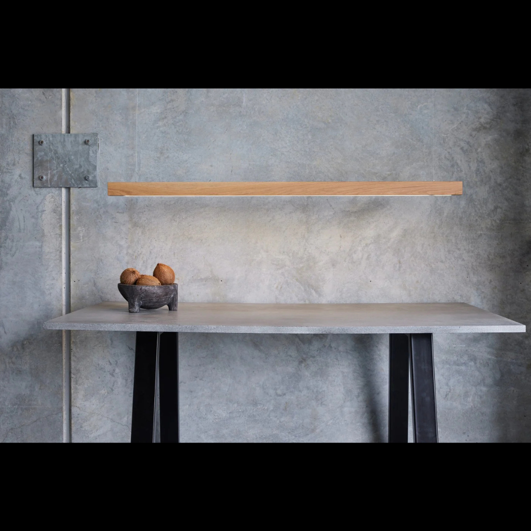 Modern interior with oak linear light, a concrete table, wooden shelf, and decorative elements against a gray wall.