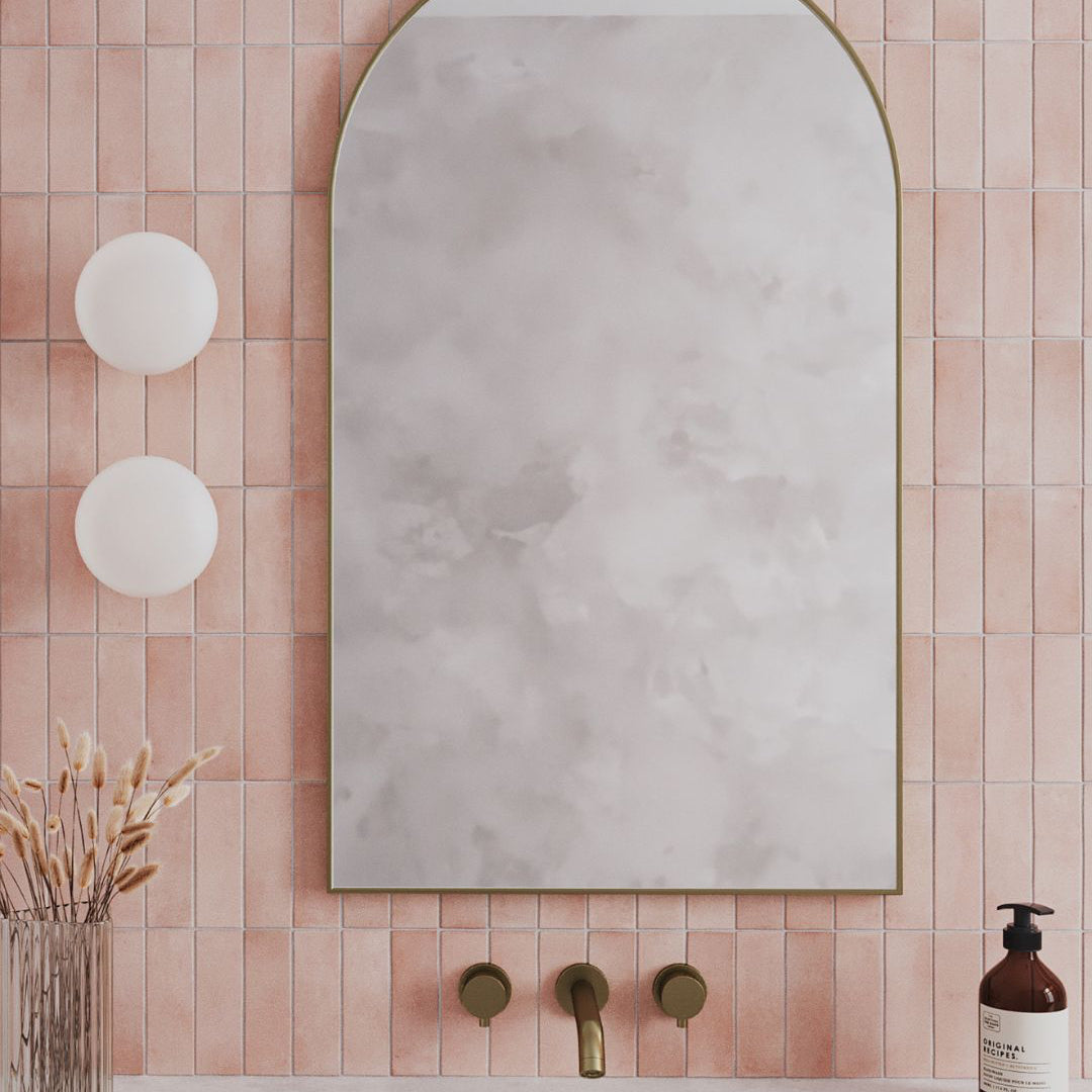 Bathroom with pink tiled walls, a mirror, sink, and bottle of soap.