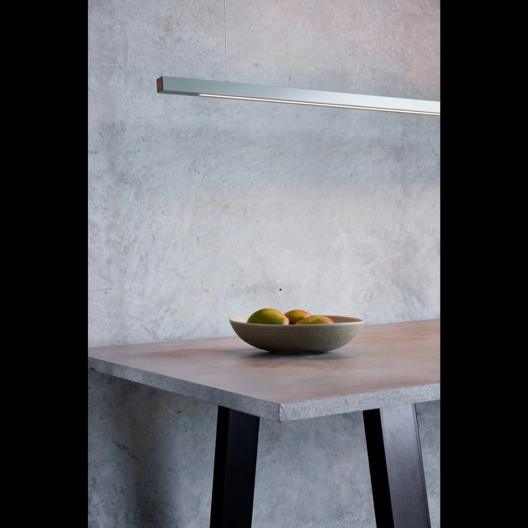 Bowl of fruit on a concrete table with a light fixture above against a gray wall.