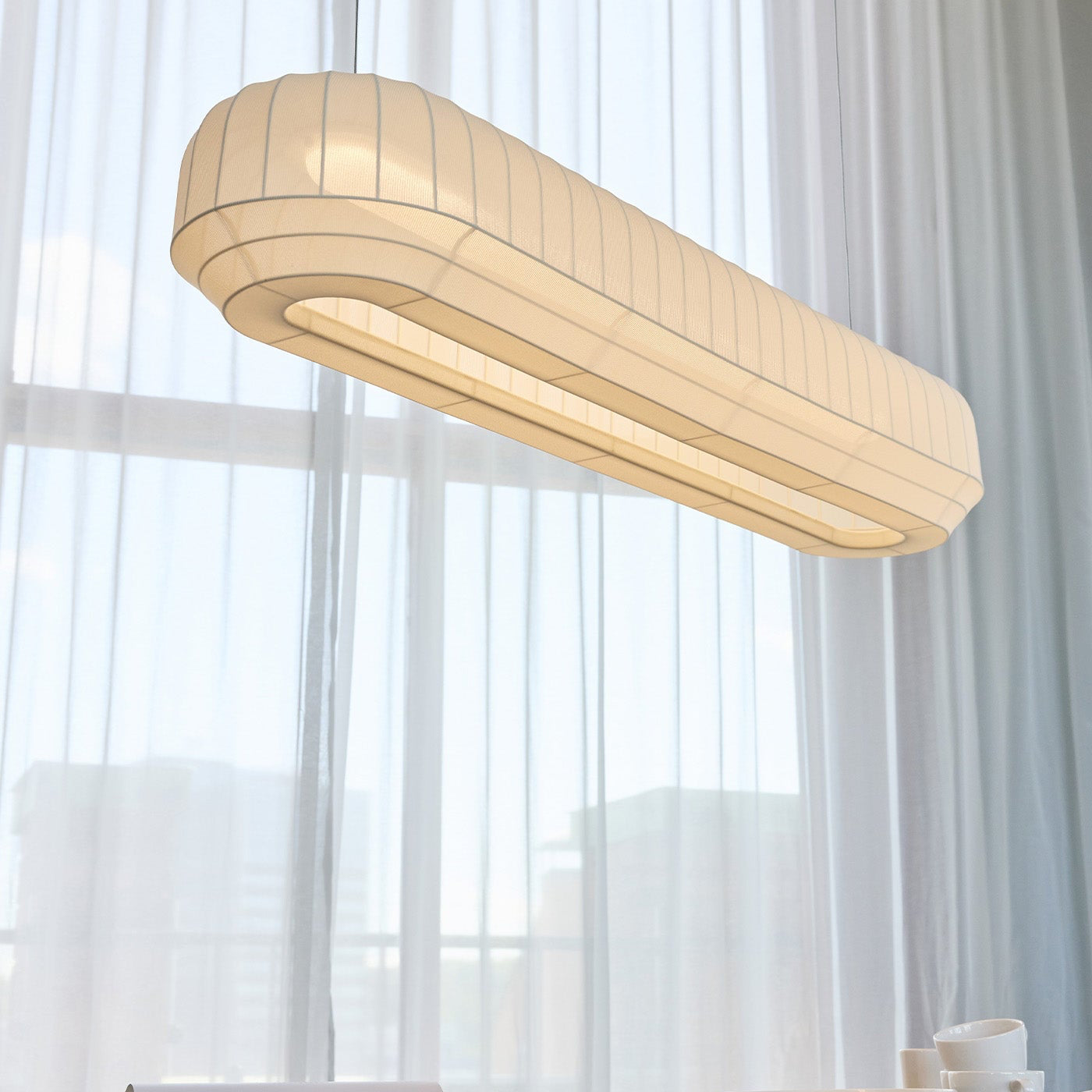 Modern pendant light hanging above a dining table with white curtains in the background