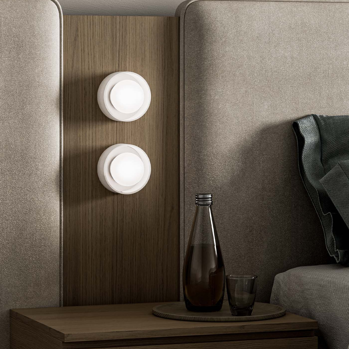 Modern wall sconces on a wooden panel next to a bed with a nightstand and decorative items.
