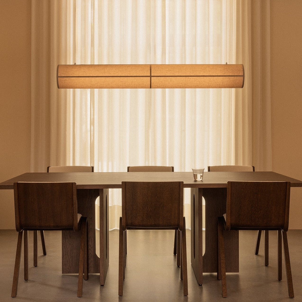 Dining table set with chairs under a long horizontal light fixture in a neutral-colored room.