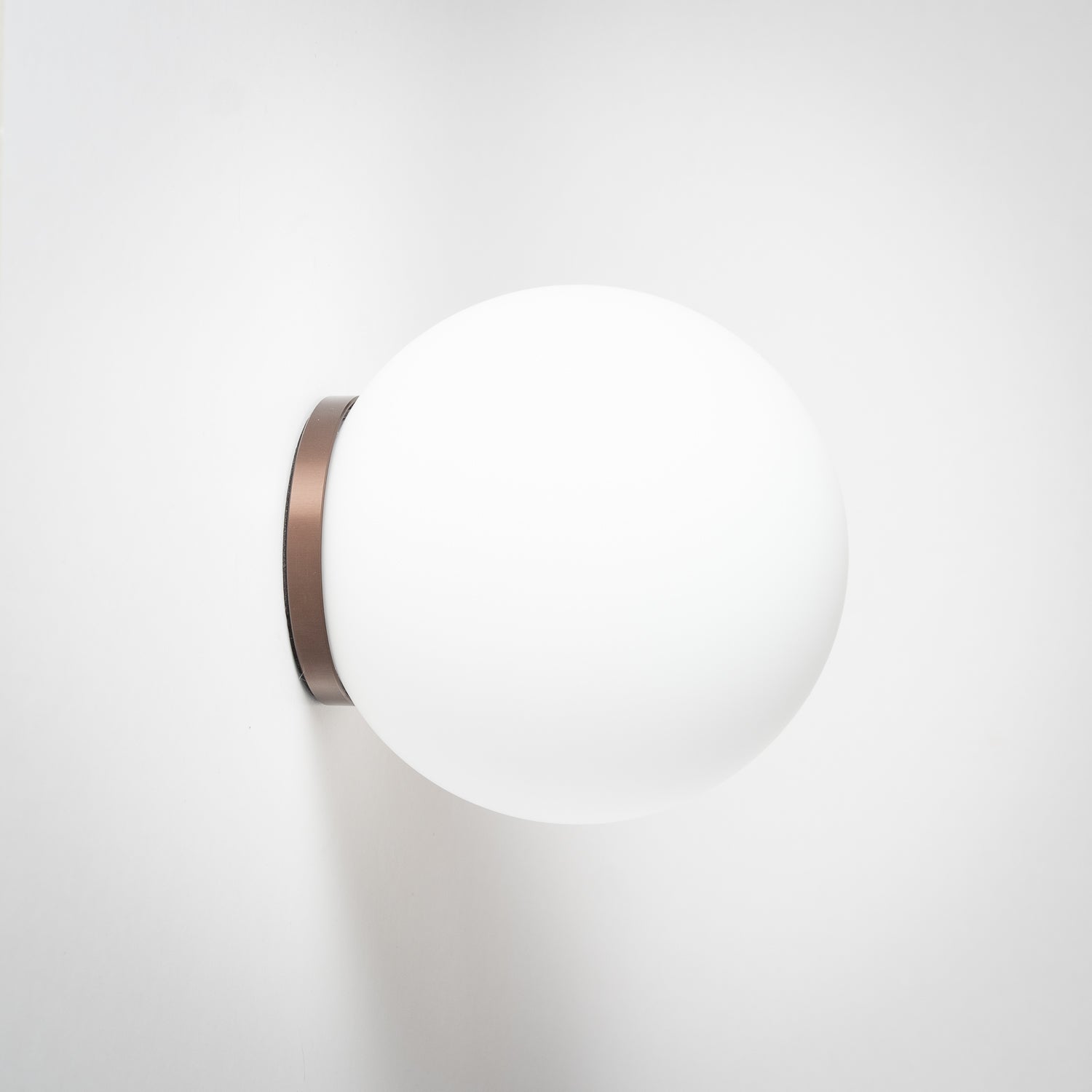 The image shows a minimalistic design wall/ceiling mount light with a round opal glass shade. There are multiple mounts visible on the wall, and the light fixtures appear in different finishes such as dark bronze, light bronze, and white.