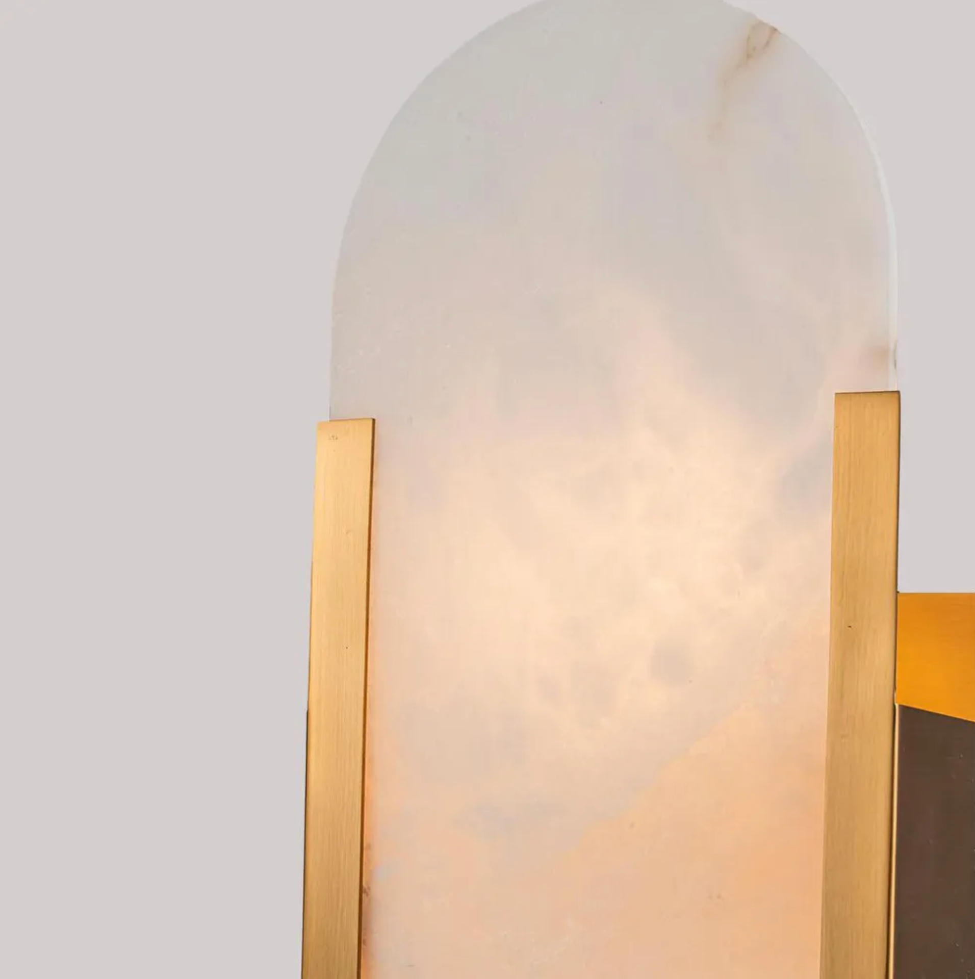 Wall-mounted light fixture with gold frame and translucent glass shade on a neutral background