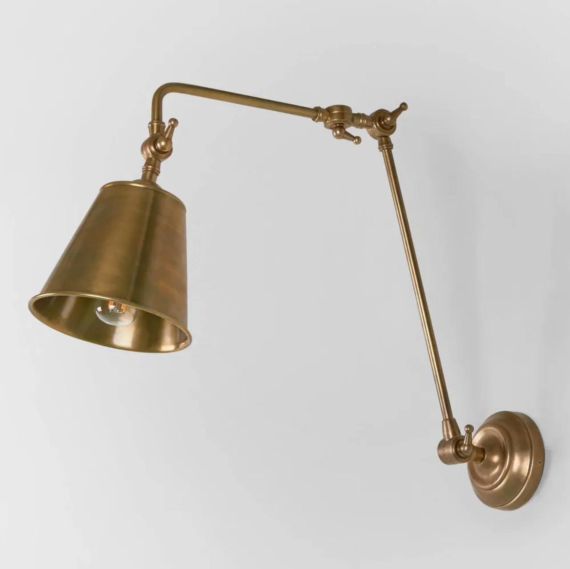 Brass wall lamp with adjustable arm on a light gray background