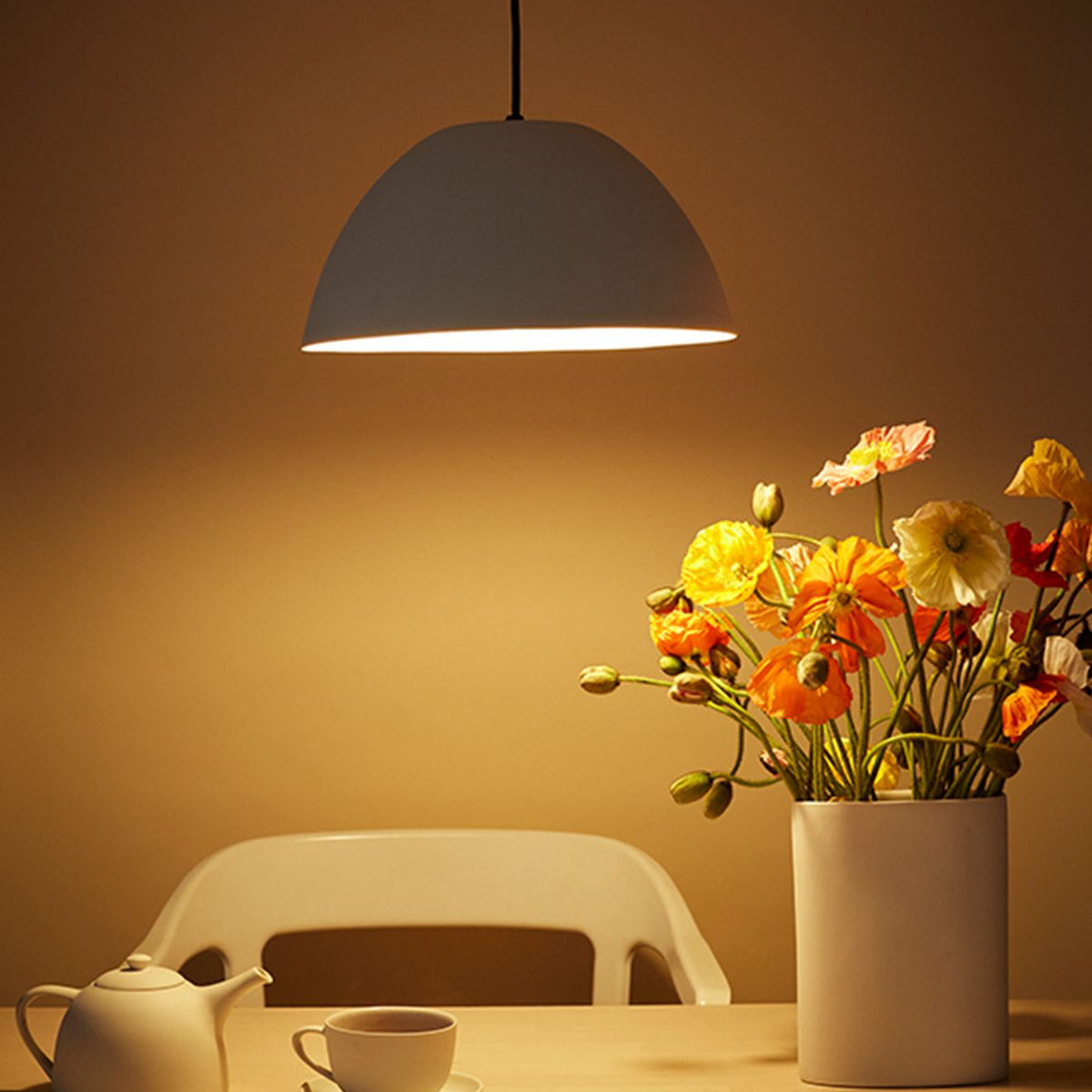 MUD Gray pendant light above a table with a teapot, cup, and vase of flowers on a warm-toned background.