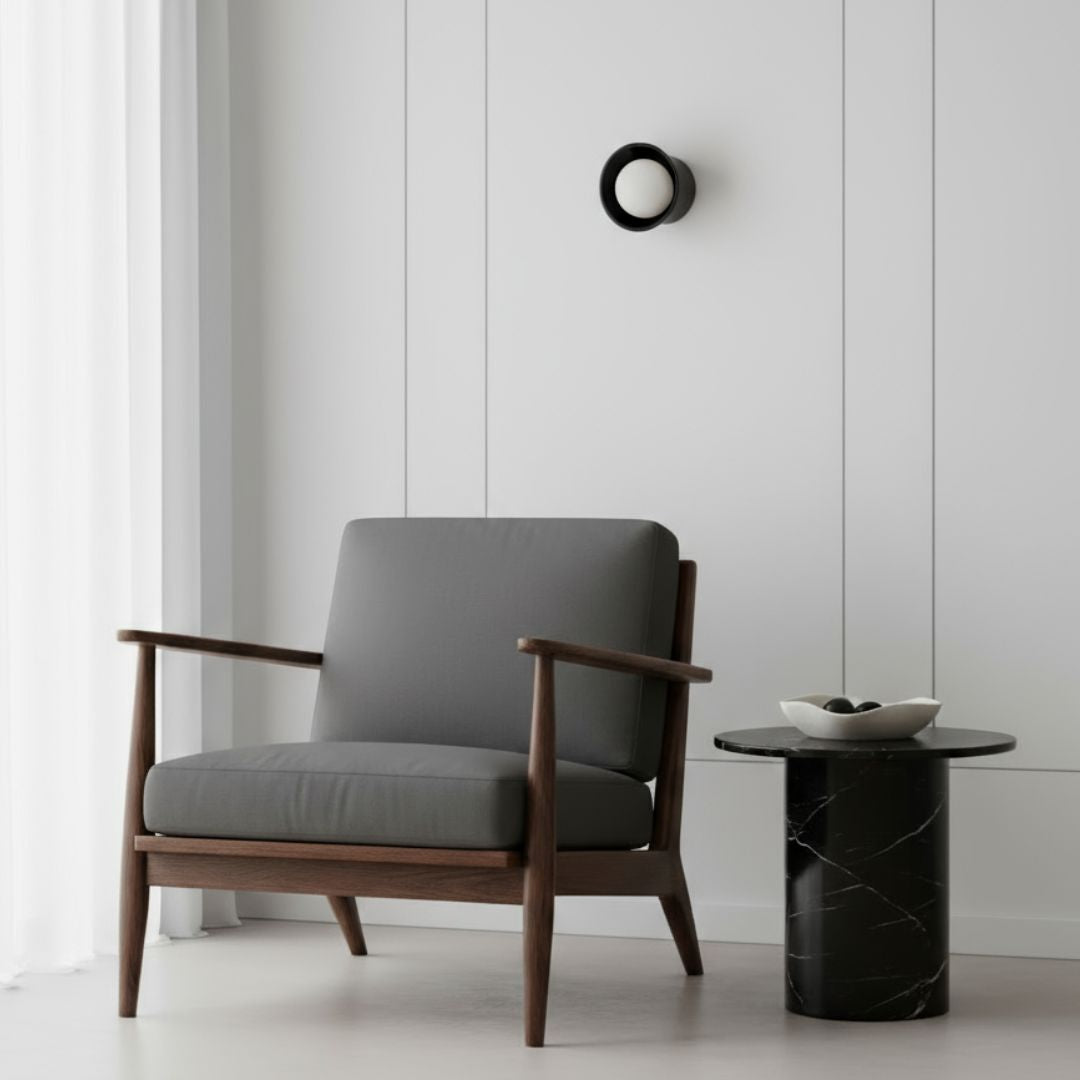 Gray armchair with wooden frame in a minimalistic room with a side table and black ceramic wall sconce